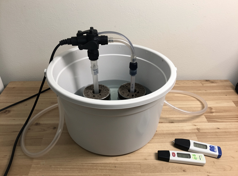 DWC air pump feeding two air stones in a reservoir with an EC pen and pH pen on the bench