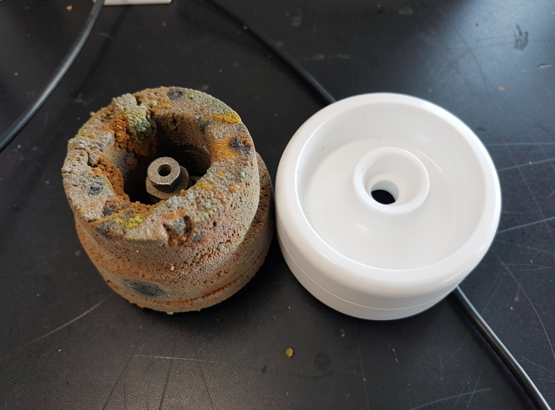 A clogged discoloured old air stone beside a clean new disc diffuser on a dark bench showing wear comparison